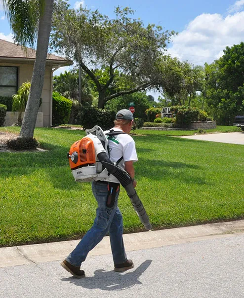 A Greenscapes crew member clearing a sidewalk with a backpack blower beside a mown verge