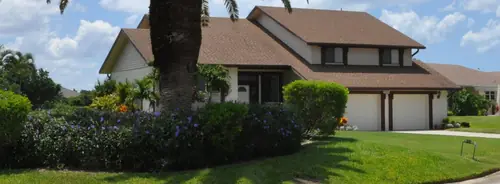 A two-storey home with a mown lawn, a tall palm and flowering shrub beds along the frontage